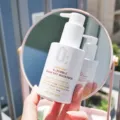 Seseorang sedang membaca label komposisi produk facial wash di depan cermin kamar mandi