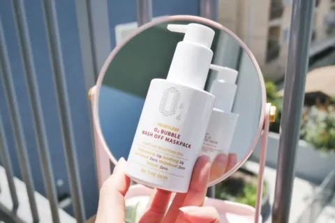 Seseorang sedang membaca label komposisi produk facial wash di depan cermin kamar mandi