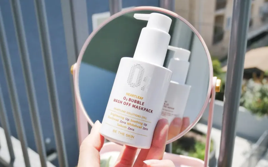 Seseorang sedang membaca label komposisi produk facial wash di depan cermin kamar mandi