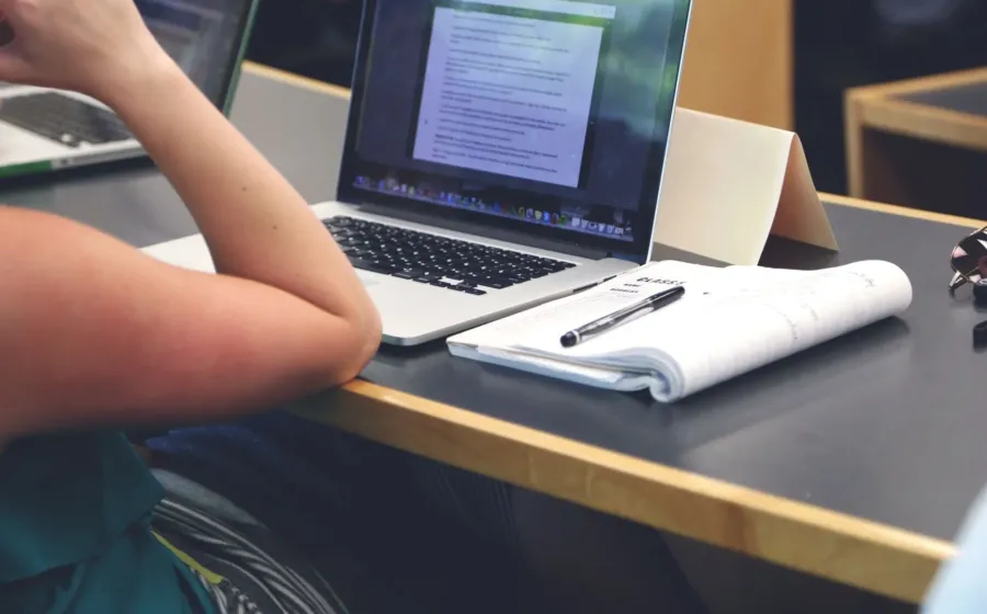 Mahasiswa sedang menggunakan laptop untuk mengerjakan tugas kuliah di lingkungan kampus