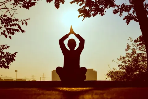 Seseorang sedang melakukan meditasi santai di alam untuk menerapkan cara menjaga pikiran tetap tenang