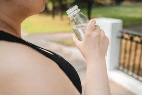 Pekerja kantor minum air putih dari botol di meja kerja untuk menjaga gaya hidup sehat yang praktis