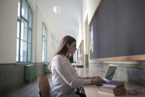 Mahasiswa sedang mengetik tugas menggunakan laptop tipis di meja perpustakaan kampus